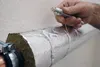 A hand is shown securing insulation around a pipe with wire. Produktbild-Vorschau
