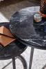 A close-up view of two nesting coffee tables with black marble-look tops and metal legs, placed on a rug. A lit candle and a notebook with a pencil are on the tables. Anteprima dell’immagine prodotto