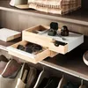 A close-up view of a wooden jewelry box with drawers, containing sunglasses and a ring box, placed on a shelf in a closet. Voir les images du produit