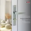 A close-up of a silver door handle on a white door, with a blurred background of a room interior. Produktbild-Vorschau