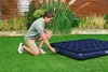 A man is kneeling on a lawn, attaching a battery-powered electric pump to an inflatable mattress. Produktbild-Vorschau