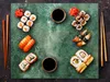 A top-down view of a variety of sushi dishes arranged on a green marble slab, with chopsticks and soy sauce. Náhľad obrázku produktu