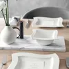 A table setting with white dinnerware, a candle, and flowers. Produktbild-Vorschau