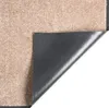 A close-up view of a beige doormat, with one corner lifted to show the dark gray backing. Voir les images du produit