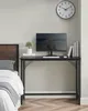 A minimalist desk with a computer and a clock on the wall, next to a bed. Náhled obrázku produktu