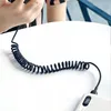 A coiled USB-C cable is connected to a white power bank on a white table. A person's hands are visible in the upper left corner, holding a black object. Anteprima dell’immagine prodotto