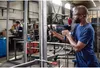 A man is using a Bosch drill in a workshop setting. Voir les images du produit