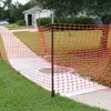 An orange plastic safety fence is set up around a concrete area in a residential yard, with a house and car visible in the background. Náhled obrázku produktu