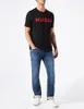 A man wearing a black t-shirt with red lettering and blue jeans, standing against a white background. Produktbild-Vorschau