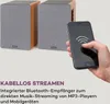 A hand holding a smartphone in front of two speakers, demonstrating wireless streaming. Produktbild-Vorschau
