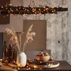 A table setting with decorative lights, dried reeds, bottles, and a bowl of nuts. Podgląd zdjęcia produktu