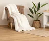 A white faux fur blanket is draped over a brown armchair, with a potted plant and a small white side table in the background. Podgląd zdjęcia produktu