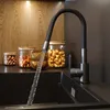 A modern kitchen sink with a black faucet with a flexible spout, with jars of nuts and wooden bowls on the counter behind it. Podgląd zdjęcia produktu