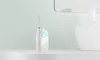 A white water flosser sits on a white shelf in front of a light green wall and a blurred sink. Náhled obrázku produktu