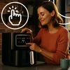 A woman is using a black air fryer in a kitchen setting. Produktbild-Vorschau