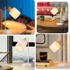 A collage of four images showing a white desk lamp with a fabric shade and wooden accents in different settings, including a bedroom, a living room with Christmas decorations, and a home office. Produktbild-Vorschau