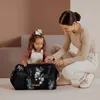 A mother and child are interacting with a black diaper bag with floral accents. Náhľad obrázku produktu