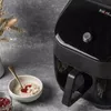 A close-up shot of an air fryer next to a bowl of oatmeal and a jar of jam. Produktbild-Vorschau