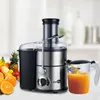 A stainless steel juicer with a pitcher of orange juice and a pile of fresh fruits in the foreground. Produktbild-Vorschau