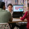 Three people are sitting around a table, looking at a laptop. Voir les images du produit