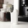 A white water filter is placed on a white surface in front of jars of coffee beans and a coffee machine. Náhľad obrázku produktu