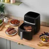 A kitchen counter with an air fryer cooking steaks and vegetables, along with side dishes. Produktbild-Vorschau
