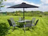 A patio table and chairs set with a large umbrella, set up on a grassy lawn with trees and a blue sky in the background. Anteprima dell’immagine prodotto