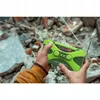 Hands holding a green emergency radio in a debris-filled environment. Produktbild-Vorschau