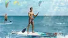 Two men are paddleboarding on a sunny day with paragliders in the sky. Náhled obrázku produktu