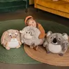 A young girl is hugging a plush sheep toy while sitting on a rug with other plush toys. Produktbild-Vorschau