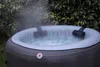 An inflatable hot tub filled with bubbling water, with steam rising, set outdoors amongst foliage. Produktbild-Vorschau