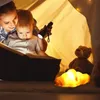 A mother and child are reading a book in a tent, illuminated by a flashlight and a croissant-shaped lamp. Podgląd zdjęcia produktu