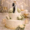 Tortenaufsatz Hochzeitspaar auf dreistöckiger Hochzeitstorte mit Blumen, Perlen und goldenen Details in elegantem Ambiente. Anteprima dell’immagine prodotto