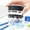A hand holding a mini desk vacuum cleaner over a pile of pencil shavings on a white desk, with a keyboard and pencils in the background. Anteprima dell’immagine prodotto