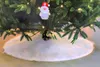 A close-up view of the base of a Christmas tree with a white faux fur tree skirt and a Santa ornament. Anteprima dell’immagine prodotto