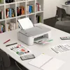 A Canon PIXMA TS3451 printer is shown on a desk in a home office or study environment, with books in the background. Podgląd zdjęcia produktu