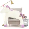A large plush unicorn is sitting on a chair next to a small table with decorative items. Podgląd zdjęcia produktu