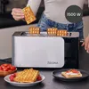 A person is placing waffles into a toaster, with finished waffles and other food items visible on the counter. Voir les images du produit