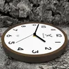 A wooden wall clock with a white face and black numbers is placed on a textured gray surface. Voir les images du produit
