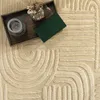 A close-up view of a textured beige rug with a geometric pattern, featuring a wooden tray with a candle and a book. Produktbild-Vorschau
