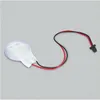 A small, circular electronic component with two wires attached, lying on a plain gray background. Produktbild-Vorschau