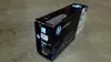 A black HP toner cartridge box is placed on a gray concrete surface. Voir les images du produit
