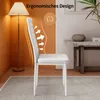 A white dining chair is shown in a room with an orange wall and a floor lamp. Náhled obrázku produktu