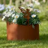 A rusty metal planter with a fairy silhouette decoration, filled with white daisies, sits on a grassy lawn. Produktbild-Vorschau