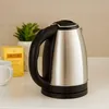 A stainless steel electric kettle sits on a countertop next to a box of tea and a mug. Náhled obrázku produktu