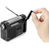 A hand is shown cranking the handle of a black emergency radio with a built-in flashlight and solar panel. Produktbild-Vorschau