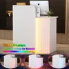 A modern white reception desk with integrated RGB LED lighting, shown in a professional setting with a computer and decorative plant. Náhľad obrázku produktu