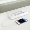 A white power strip with multiple outlets and USB ports is shown on a white surface, with a smartphone connected to it via a white cable. Náhled obrázku produktu