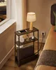 A bedside table with a lamp, phone, and blanket next to a bed and a window with a view of a landscape. Náhled obrázku produktu