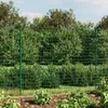 A green wire mesh fence in a garden setting with plants in the foreground and trees in the background. Náhled obrázku produktu